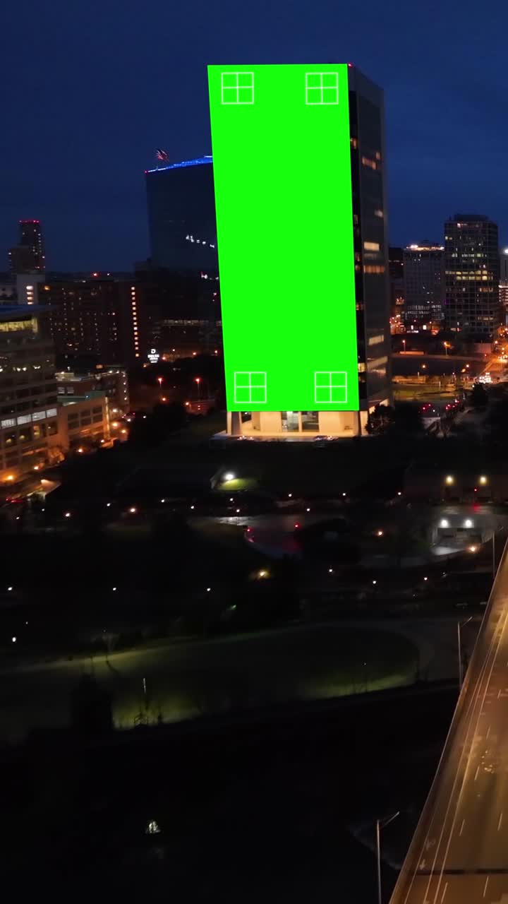 Valla publicitaria con pantalla verde para publicidad en un edificio de noche. Mockup y concepto de marketing digital para promoción de la ciudad. Aérea. Clip vertical