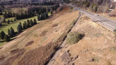 2-4 aerial fly over city valley river golf course next to an ungroomed park while couple social distance from each other as they walk on the path paved concrete by the roadside residential community