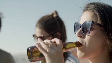 close up of a caucasian woman in sunglasses drinking beer from bottle at party