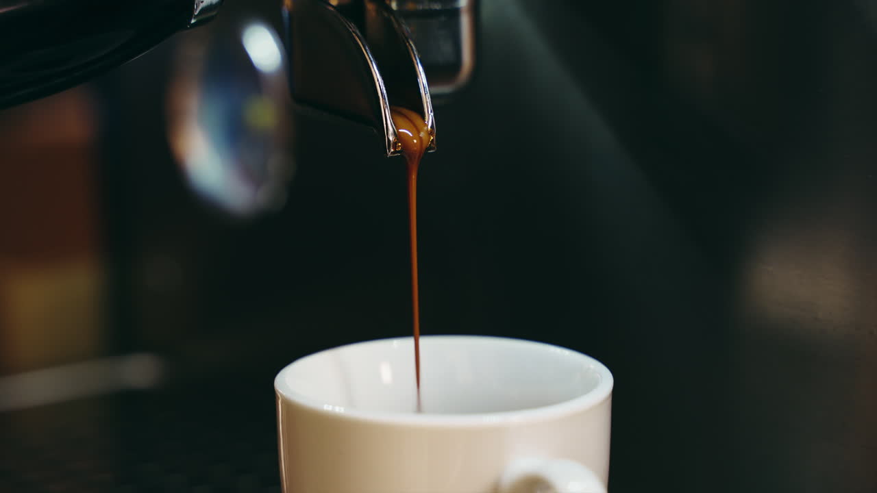Um plano médio-fechado de café sendo despejado de uma máquina de café em uma xícara branca.