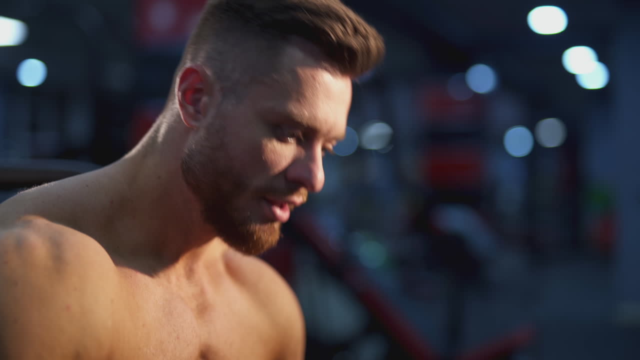 Handsome sportsman resting after hard training. Portrait of a young shirtless athlete breathing hard after doing workout in the gym. Close-up.