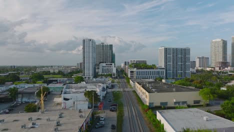 elevated view of green vegetation and buildings in city. vehicles driving on road and crossing railway tracks. miami, usa