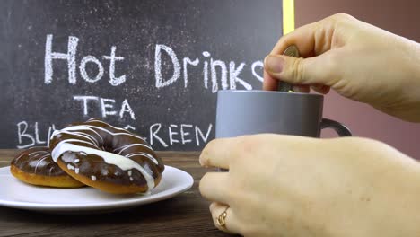 female hands holding a cup of tea and stirring with a spoon.menu stand in the background.