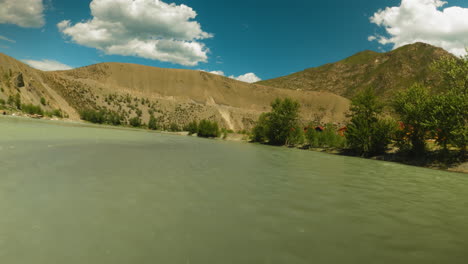 calm river runs slowly past trees in hill valley fpv. powerful water flow surrounded by lush greenery against old mountain ridge. nature majesty