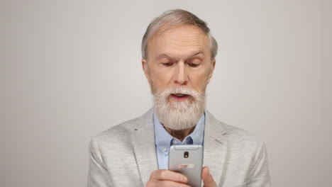 Mature-man-looking-to-smartphone-in-studio.-Old-guy-using-cellphone-inside.