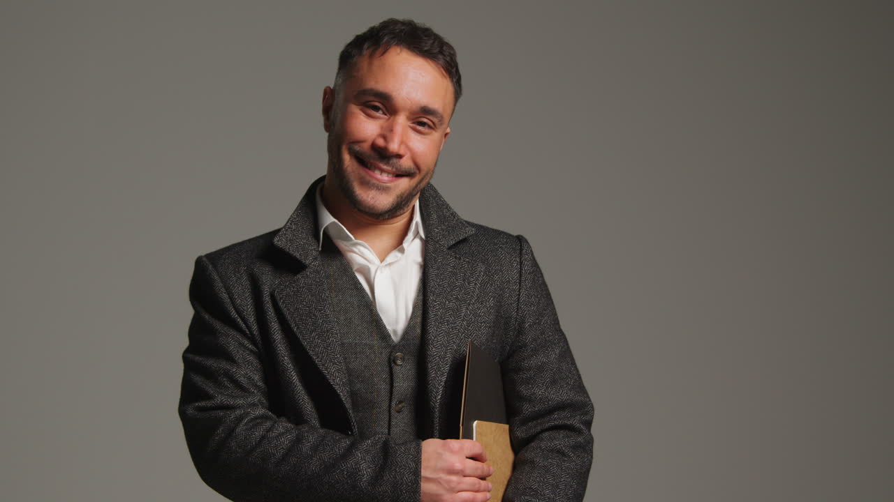 hombre sonriente con un abrigo sosteniendo un libro