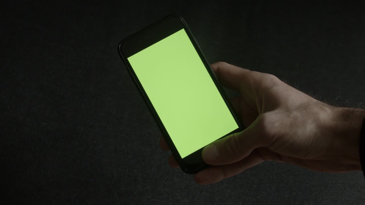 mano di uomo che tiene un cellulare con schermo verde su uno sfondo nero