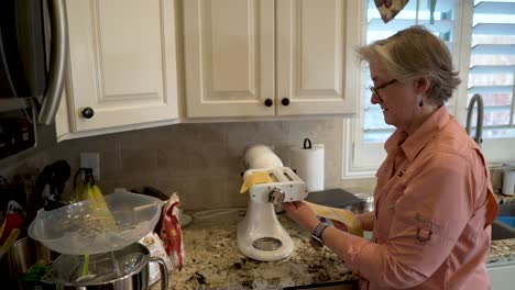mujer madura extendiendo una lámina delgada de masa para pasta en un accesorio para hacer pasta