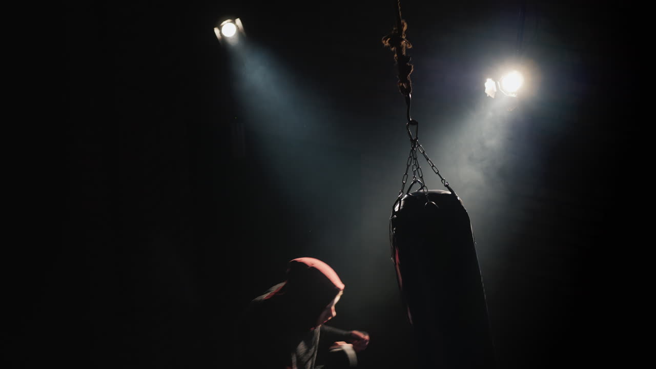Silhouette di un combattente Trinity in palestra - colpisce un sacco da boxe.
