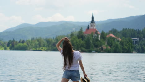 woman enjoying a scenic view of a lake with mountains and a church in the background.