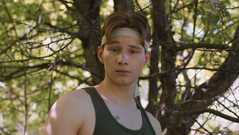 front view soldier dodging thin dry branch while winking and giving thumbs up to camera under leafy canopy expressing confidence and relief during forest exploration and playful adventure