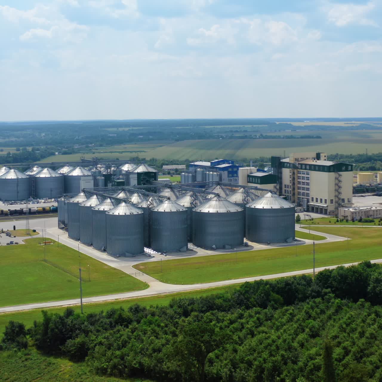 Modern plant on field. Silver silos on agro-processing and manufacturing plant for processing agricultural products. Aerial view. Motion camera back