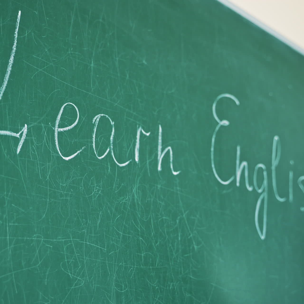 Close-up of a hand with a chalk writing the word English. Woman's hand holding chalk and writing the words Learn English on the green board.