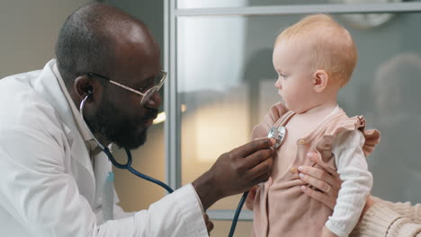 mother holding baby while pediatrician giving checkup with stethoscope