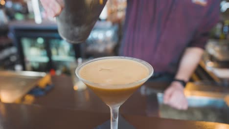 pouring last drop of espresso martini from shaker with hawthorne strainer, bartender
