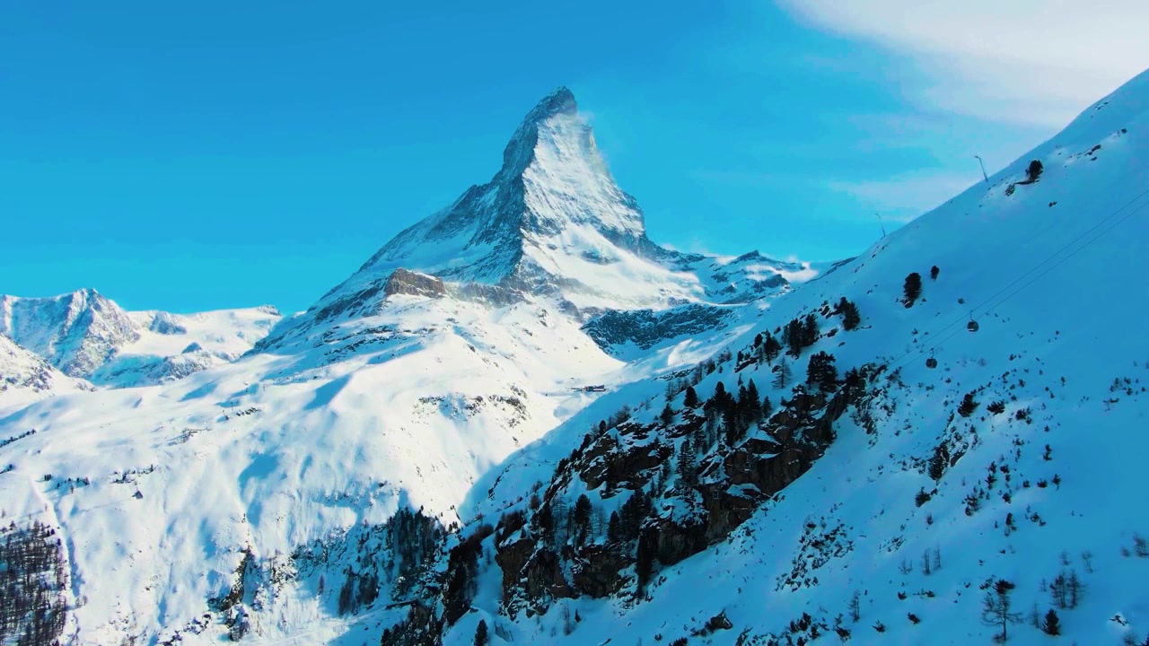 Eine atemberaubende, filmische Luftaufnahme, die den ikonischen, zerklüfteten Pyramiden-Gipfel des schneebedeckten Matterhorns einfängt, der majestätisch über der unberührten alpinen Winterlandschaft aufragt