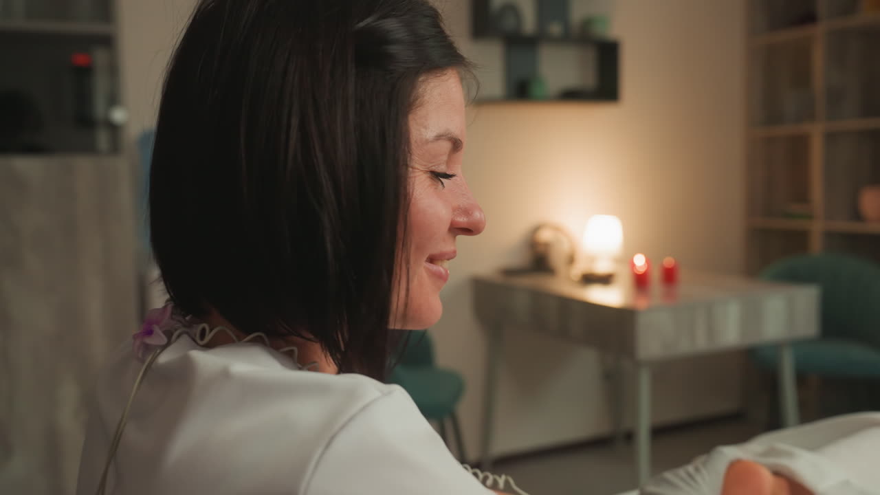 Caucasian esthetician performing microcurrent hand therapy, cozy spa room lit by candlelight, gloved practitioner attaches electrode gloves to clients forearm, gentle pulsing and massage motions