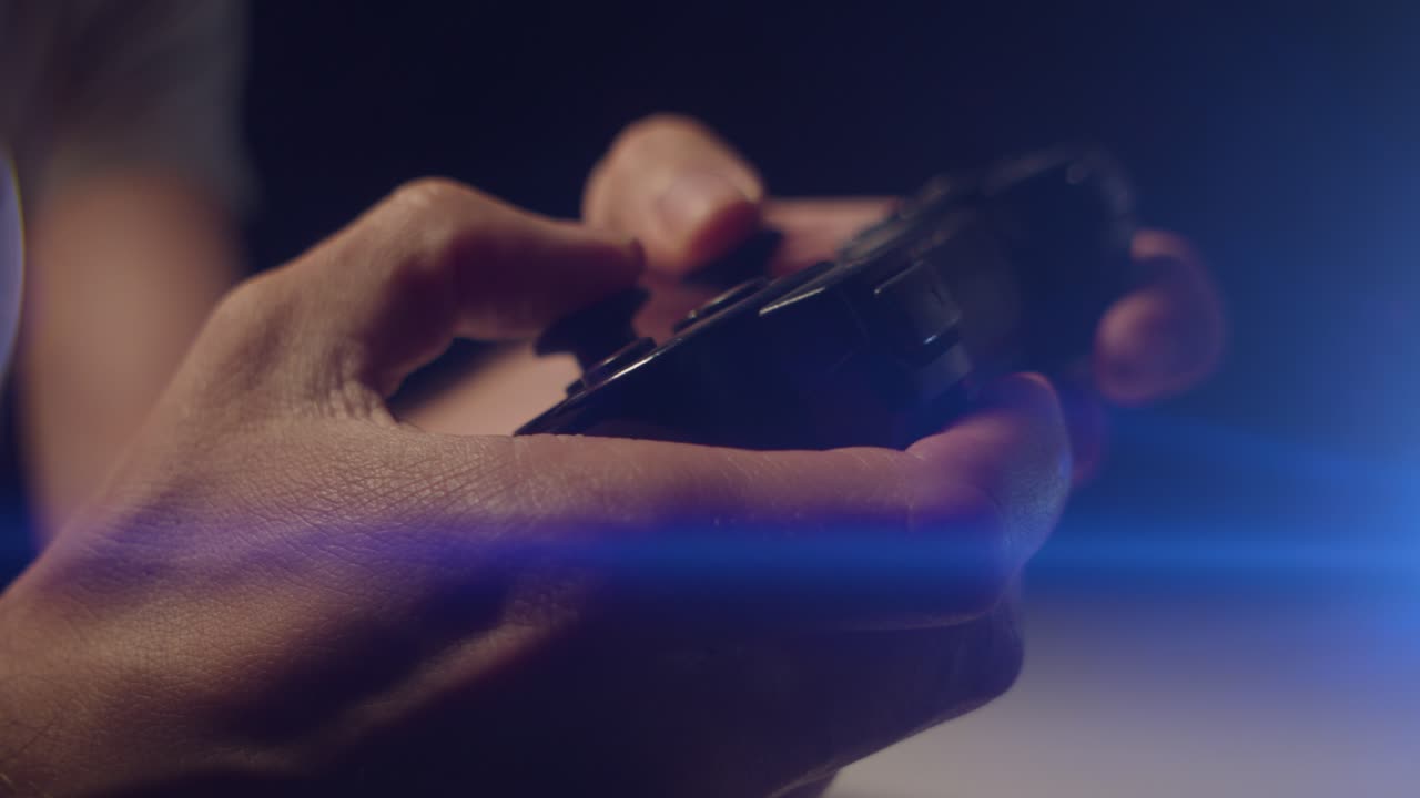Playing video games in a darkened room with an anamorphic lens flare on a small controllers buttons playing slowly close up