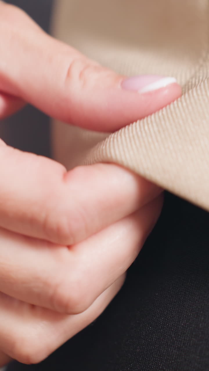 Белый инспектор ощупывает текстуру и кромку ткани бежевого цвета, женщина европеоидной расы проводит пальцами по тканому переплетению и шву, студийные крупные планы переплетения и отделки, тактильный контроль качества и качественная отделка