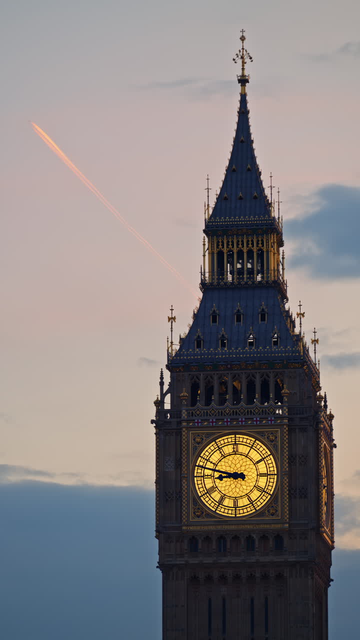 Close-up view of Big Ben illuminated at dusk with airplane passing by in London, England. Vertical