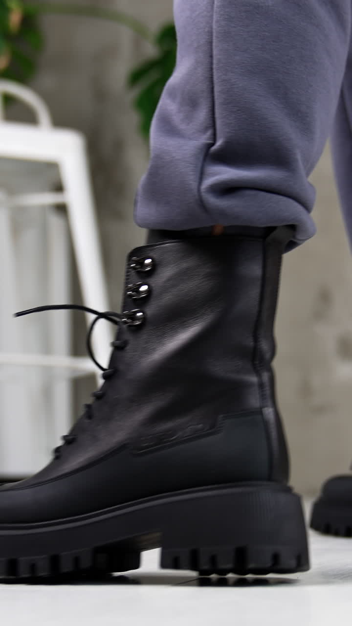 Black laced army boots demonstration. Close up. Model wearing grey pants and leather massive footwear in studio. Vertical video