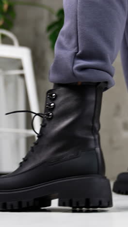 black laced army boots demonstration. close up. model wearing grey pants and leather massive footwear in studio. vertical video