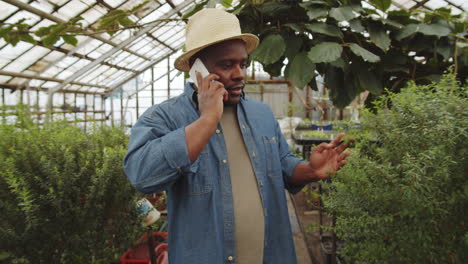 black farmer walking in greenhouse and talking on phone