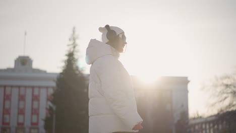 radiant sunlight shines on young woman dancing joyfully in winter attire, full of youthful spirit and graceful jiving motion, as warm glow creates serene atmosphere across snow-lined urban steps