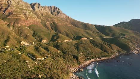 waves-crashing-on-mountain-beach-in-Cape-Town-at-Chapmans-Peak-during-sunset,-aerial