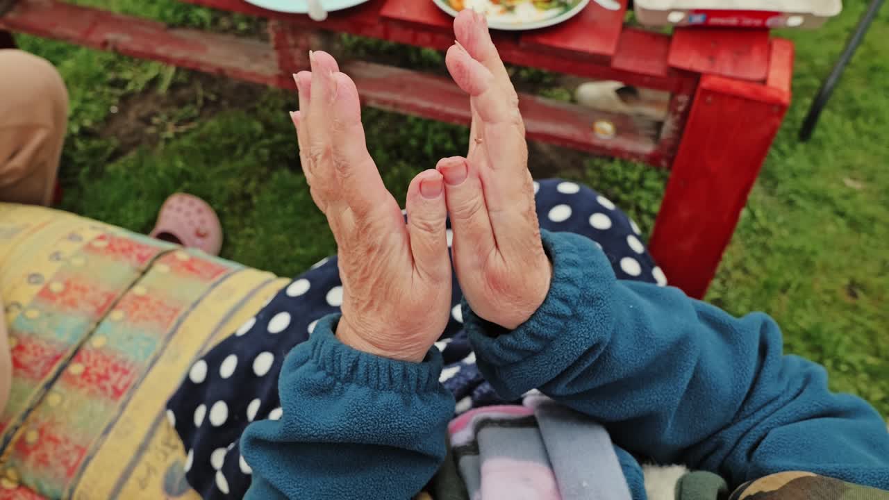 Senior claps gently in layered clothing, colors of cozy spring garden, Latvia
