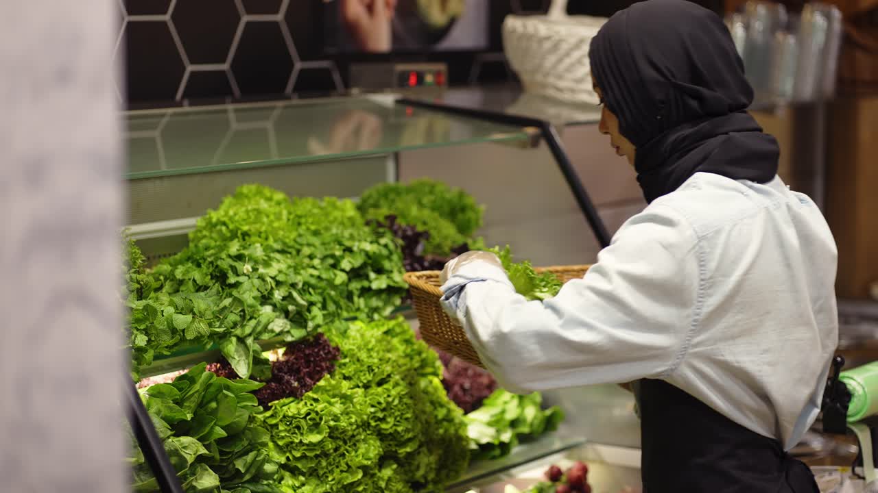 женщина в шарфе заполняет свежие зелень на полке в супермаркете