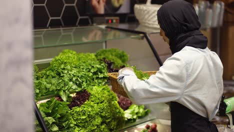 Woman-in-scarf-refill-the-fresh-greens-on-the-shelf-at-the-supermarket
