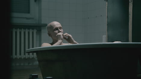pale bald skinny man takes a bath in the creepy old bathroom at night