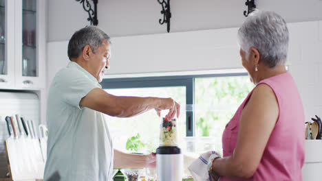 Happy-senior-biracial-couple-preparing-healthy-drink-in-kitchen