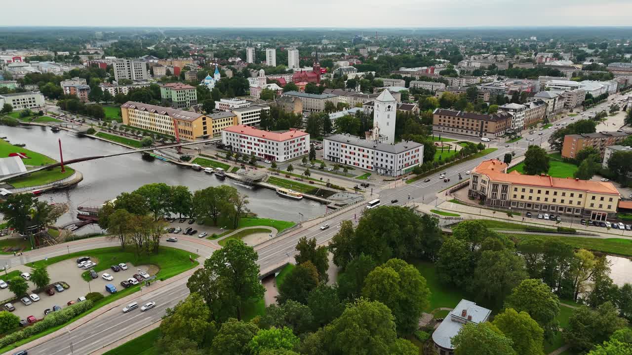Drone establishing shot over Jelgava, Latvia reveals Brīvības bulvāris, Lielupe River, and iconic civic buildings including Jelgava Palace and Holy Trinity Tower, framed by urban greenery and bridges