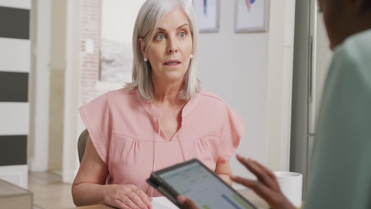 Happy senior caucasian woman with african american female friend using tablet