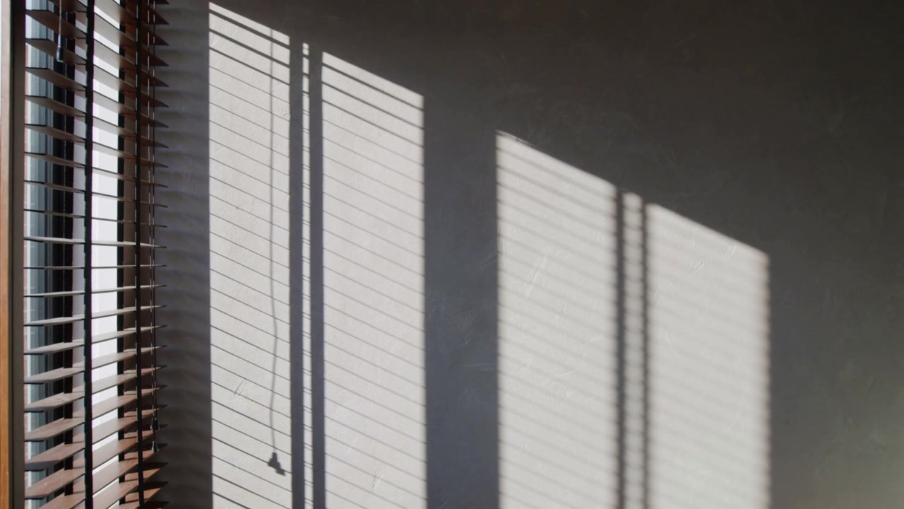 Shifting sunlight sliding across painted wall at home, wooden blinds and cord showing sun shift
