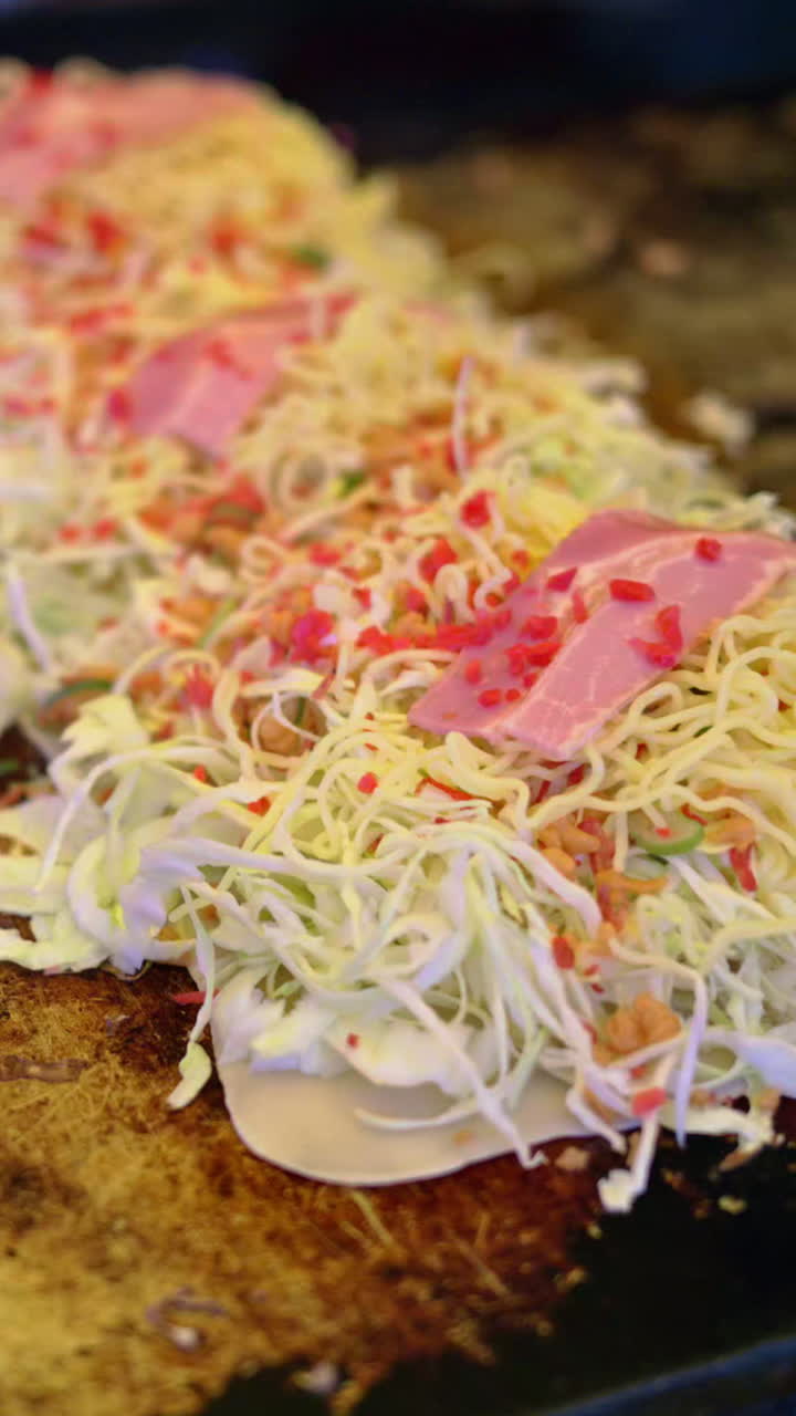 Close up of Okonomiyaki, Japanese cabbage pancakes being cooked at a street food market in Japan. Vertical