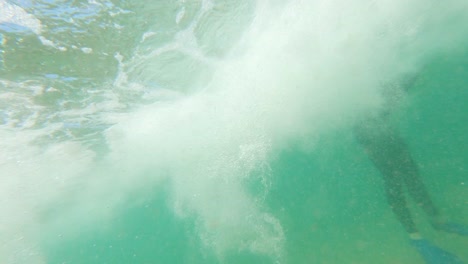 una toma en cámara lenta debajo del agua de una ola rompiendo a un bodyboarder sentado en el surf