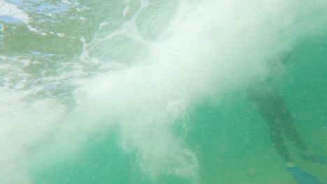 a slow motion shot from under the water of a wave breaking to a bodyboarder sitting out in the surf