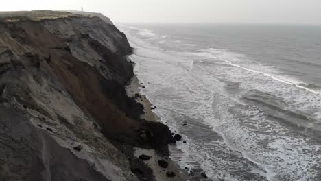 Vista-Aérea-Del-Faro-Y-Las-Empinadas-Laderas-De-Rubjerg-Knude-Junto-Al-Mar-Del-Norte,-Dinamarca