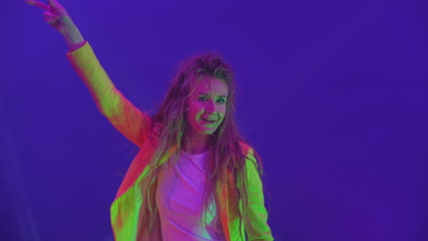 the woman dances merrily and looks at the camera in the light of strobe lights and spotlights. neon colors and crazy girl dancing to music and singing