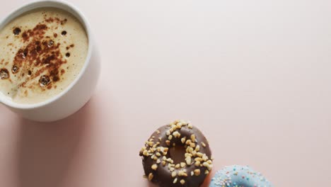 Video-of-donuts-with-icing-and-cup-of-coffee-on-pink-background