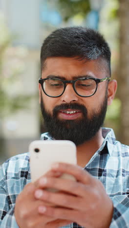 Indian-bearded-man-using-smartphone-typing-text-messages-in-social-media-application-online