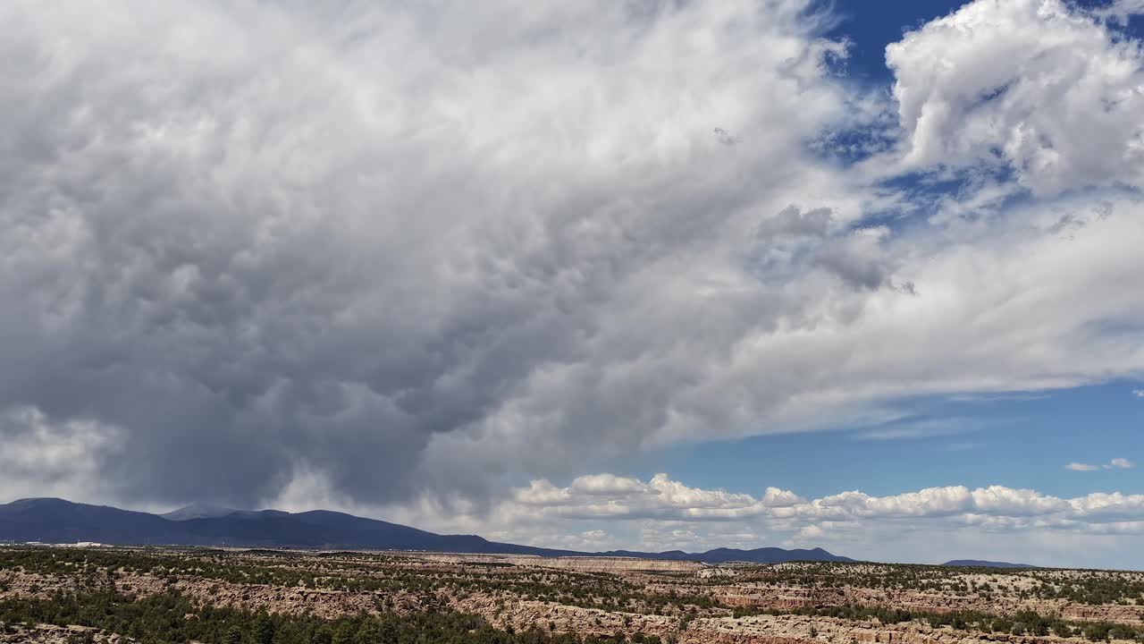 Un drammatico volo di drone in timelapse 4K scivola su aspre mesas desertiche. Nuvole temporalesche monsoniche si formano e piove simultaneamente su un lontano orizzonte montuoso nel Sud-ovest.