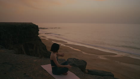 woman meditating on a cliff at sunset