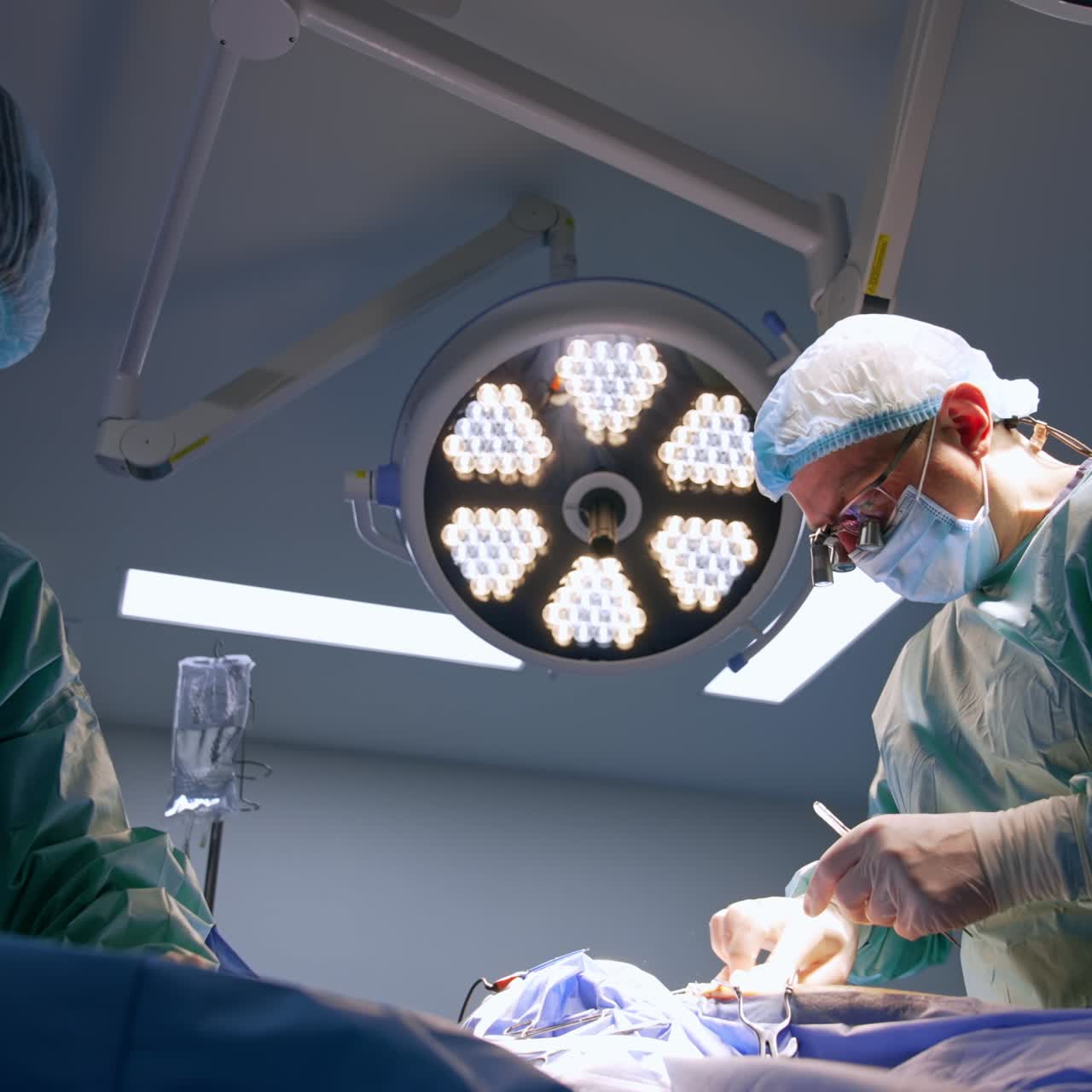 Un médico termina la operación cosiendo la incisión. Una enfermera corta el hilo quirúrgico con unas tijeras. Perspectiva de ángulo bajo.