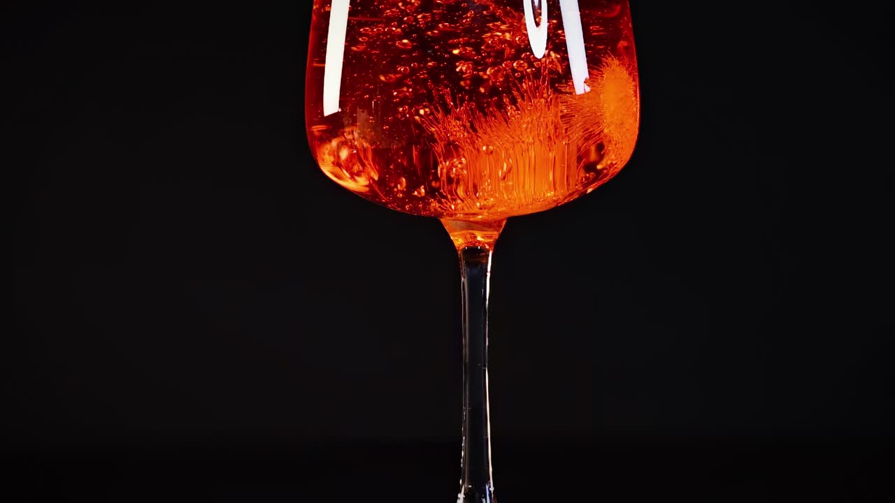 Eine Bilderserie, die eine orangefarbene Flüssigkeit mit Blasen in einem Glas vor dunklem Hintergrund zeigt.