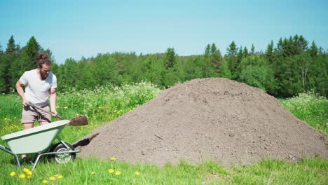 man at work shoveling soil into wheelbarrow at the farm in spring