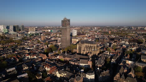 vista aérea lateral de la torre de la catedral medieval de dom en andamios en el centro de la ciudad holandesa de utrecht que se eleva sobre el paisaje urbano contra un cielo azul amanecer y un resplandor naranja en el horizonte
